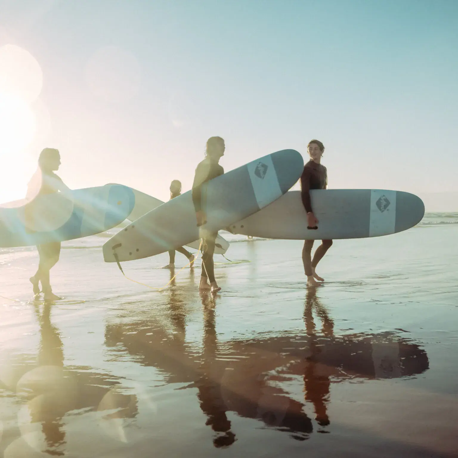 Peaceful beach scene with people carrying surfboards at sunset